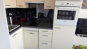 A compact kitchen with a dishwasher, oven, and stovetop. - Cozy Studio for 2 with A/C, Pool Access, & Parking in Agde (Cap d'Agde naturisme)