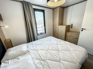 Makuuhuone, jossa on sänky, vaatekaappi, ikkuna verhoilla ja kattovalaisin.