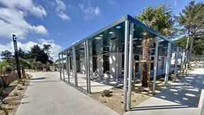 Eine moderne Glasarchitektur mit Metallgerüst, umgeben von einer Schotterfläche und einem Betonweg.