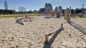 Ein Sandspielplatz mit Holzspielgeräten und einer Rutsche.