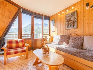 Una cabaña acogedora con interiores de madera, un sofá, un sillón a cuadros y una mesa.