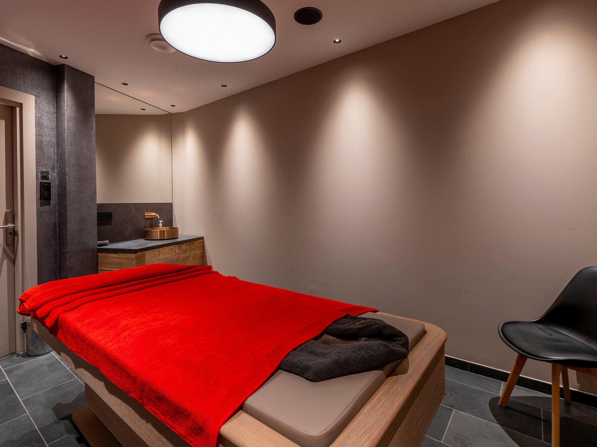 A modern bedroom with a bed, a chair, and a small vanity with a mirror.