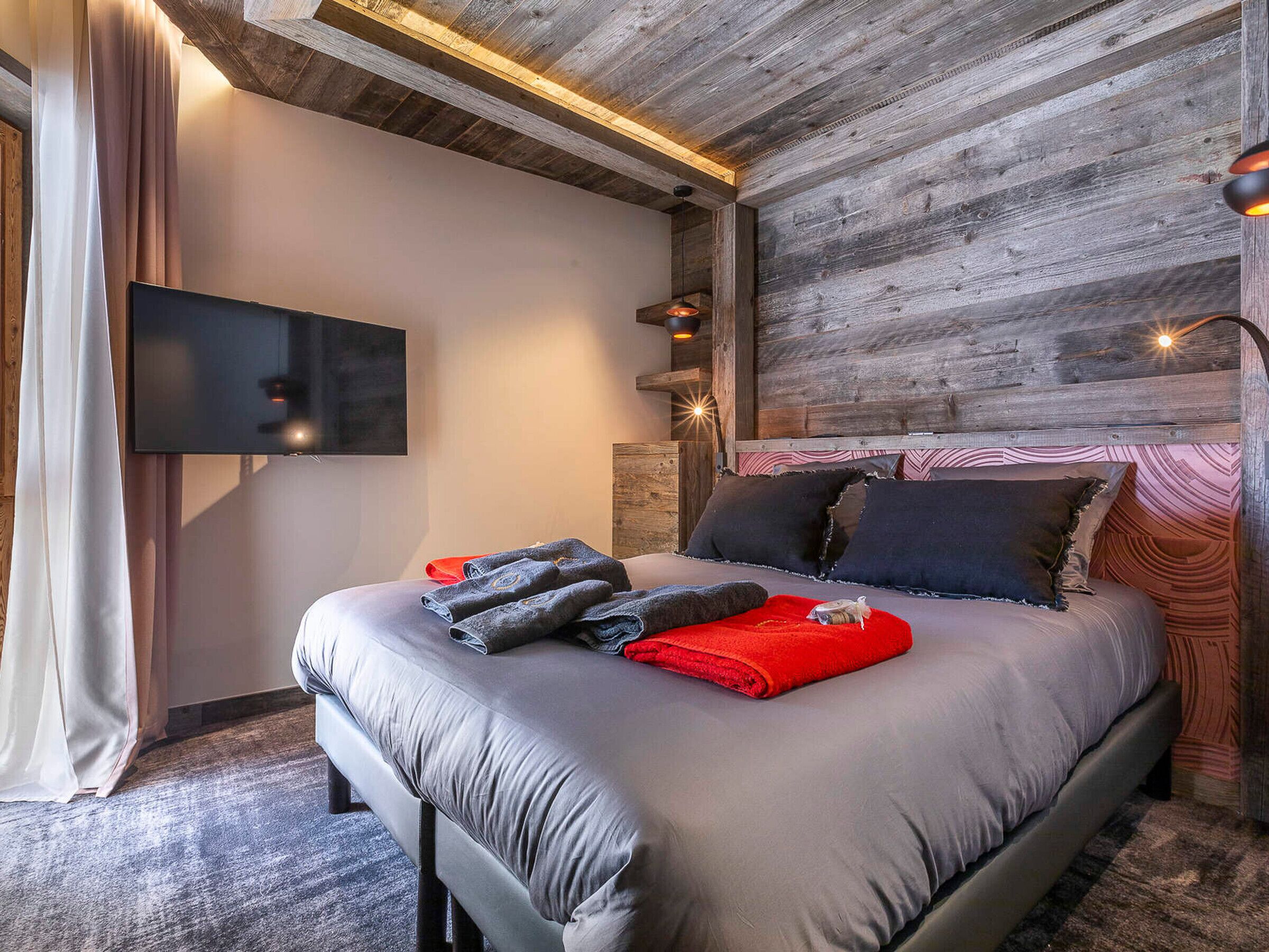 Ein modernes Schlafzimmer mit einem großen Bett, einem Flachbildfernseher und einer Holzbalkendecke.
