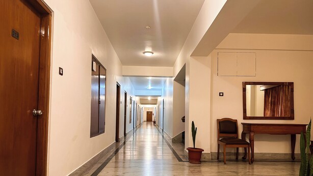 A hotel hallway with a marble floor, wooden doors, and a seating area with a mirror and potted plants. - lhaki Hotel (Phuntsholing)