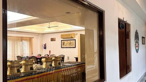 A hallway with a large mirror reflecting a dining area, a ceiling fan, and a wall-mounted fire extinguisher. - lhaki Hotel (Phuntsholing)
