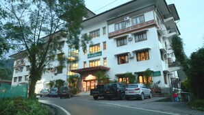 A multi-story hotel with a traditional architectural style, featuring a prominent entrance and several parked vehicles in front. - lhaki Hotel (Phuntsholing)