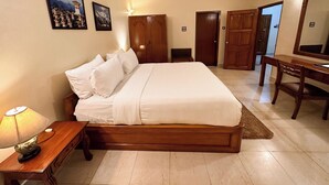 A bedroom with a large bed, wooden wardrobe, desk, and a ceiling fan. - lhaki Hotel (Phuntsholing)