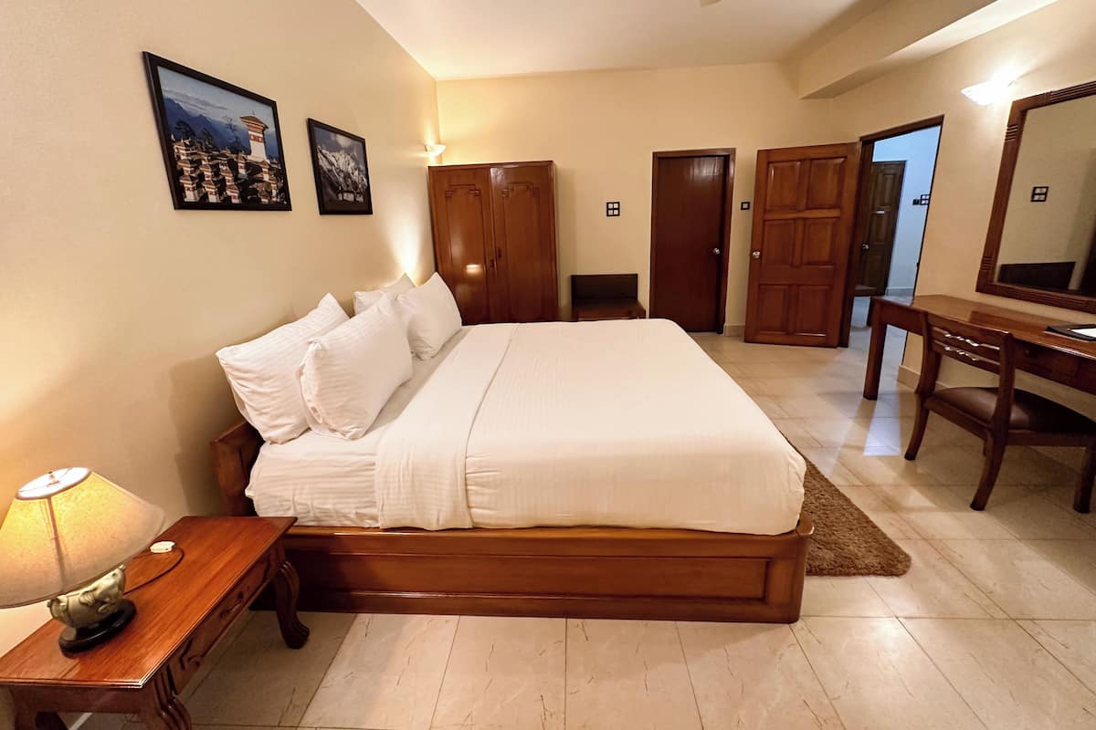 Une chambre avec un grand lit, une armoire en bois, un bureau et un ventilateur de plafond.