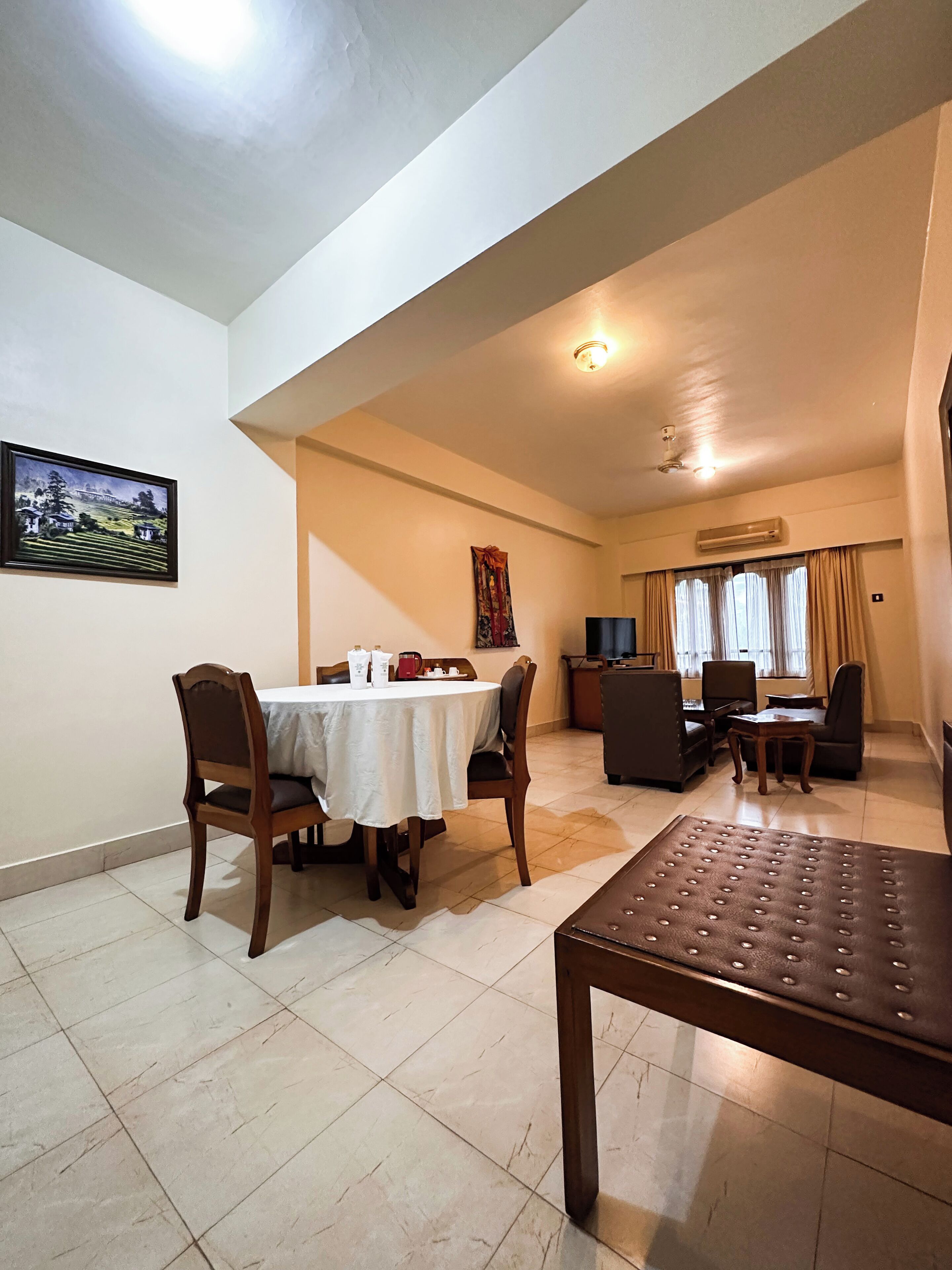 A dining area with a table and chairs, a sofa, a TV, and a small table with a lamp.