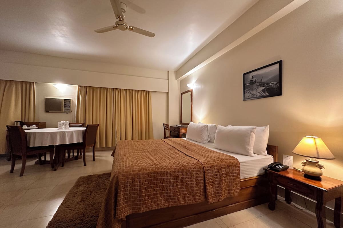 Une chambre d’hôtel équipée d’un lit, d’un bureau, d’une chaise, d’une table, d’une lampe et d’un ventilateur de plafond.