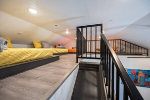 Un dormitorio tipo loft con escalera, piso de madera y cama con colcha amarilla.