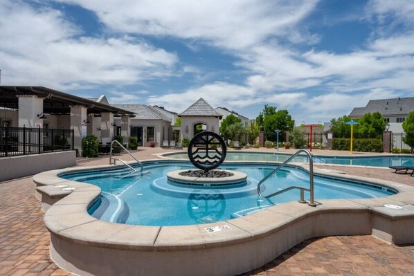 A swimming pool with a decorative centerpiece, surrounded by a brick patio and adjacent buildings.