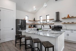 A modern kitchen with a marble island, bar stools, white cabinetry, and built-in appliances.