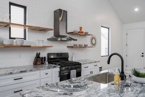 Una cocina moderna con armarios blancos, estufa de acero inoxidable y encimeras de mármol.