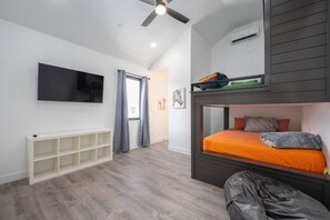 A room with a bunk bed, a flat-screen TV mounted on the wall, a ceiling fan, and a window with curtains.