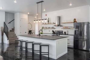 A modern kitchen with a central island, stainless steel appliances, and a staircase leading to another level.