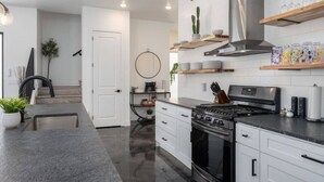 Cocina moderna con estufa, horno y campana extractora de acero inoxidable. Hay armarios blancos, una encimera y una planta en maceta.