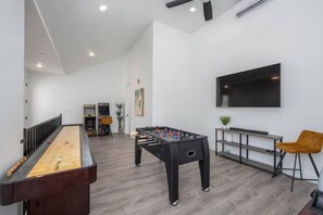 A room with a foosball table, a shuffleboard table, and a television mounted on the wall.