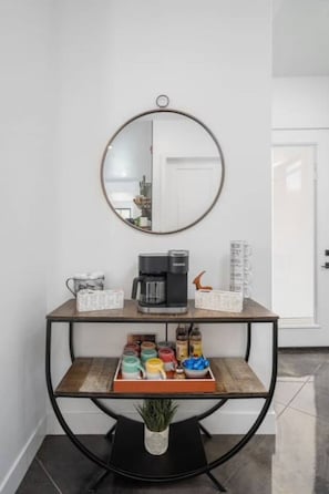 A coffee station with a coffee maker, a tray of mugs, and a variety of coffee pods.