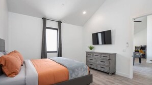 Un dormitorio moderno con cama, cómoda gris y televisor en la pared.