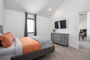 A modern bedroom with a bed, a dresser, and a TV mounted on the wall.