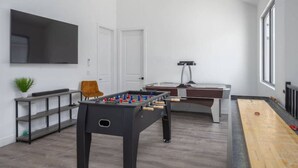 Una sala de estar moderna con mesa de fútbol, mesa de billar, televisor de pantalla plana montado en la pared y ventilador de techo.