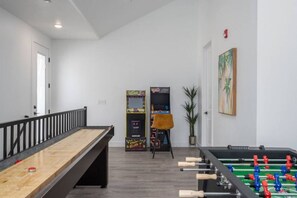 A billiards table, a foosball table, and a bookshelf in a room with white walls and a wooden floor.