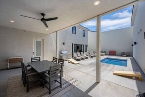 Une terrasse couverte avec une table à manger, des chaises, un barbecue, des fauteuils et une piscine.
