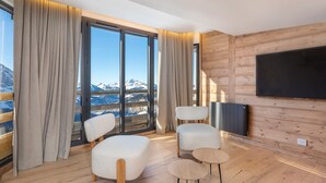 A modern room with large windows, a flat-screen TV, and two white chairs with wooden legs. - Stunning 4-room duplex for 10 in Avoriaz with ski-in/ski-out access (Avoriaz)