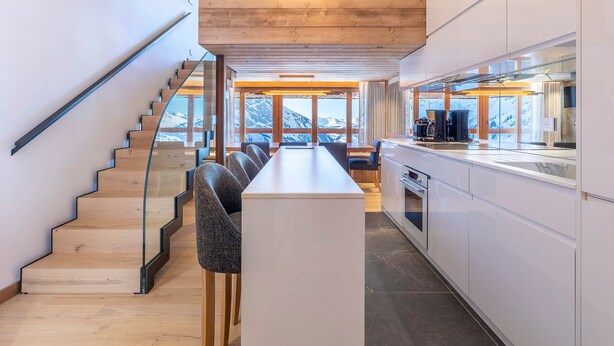 A modern kitchen with a wooden staircase, a bar area, and large windows offering mountain views. - Stunning 4-room duplex for 10 in Avoriaz with ski-in/ski-out access (Avoriaz)