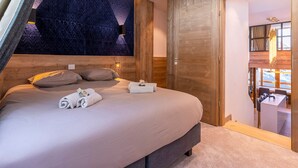 A modern hotel room with a large bed, wooden paneling, a geometric wall design, and a view of the mountains through the window. - Stunning 4-room duplex for 10 in Avoriaz with ski-in/ski-out access (Avoriaz)
