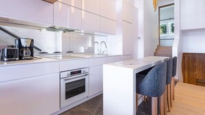 A modern kitchen with white cabinetry, a built-in oven, a coffee maker, and a dining area with a bar stool. - Stunning 4-room duplex for 10 in Avoriaz with ski-in/ski-out access (Avoriaz)
