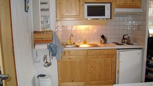 A compact kitchen with wooden cabinets, a microwave, a sink, and a small refrigerator. - Ski-in/Ski-out Apartment, 2 Bedrooms, Sleeps 4, Balcony, Parking, Crest-Voland (Crest-Voland)