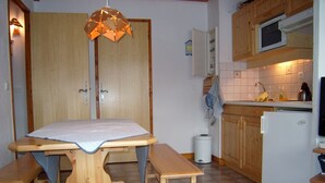 A compact kitchen with wooden cabinets, a microwave, a refrigerator, and a dining table with benches. - Ski-in/Ski-out Apartment, 2 Bedrooms, Sleeps 4, Balcony, Parking, Crest-Voland (Crest-Voland)