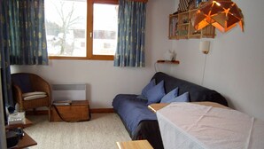 A cozy room with a bed, a chair, a small table, and a window with curtains. - Ski-in/Ski-out Apartment, 2 Bedrooms, Sleeps 4, Balcony, Parking, Crest-Voland (Crest-Voland)