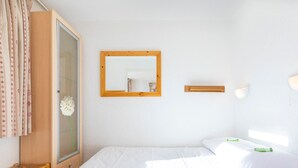 Ein Schlafzimmer mit einem Bett, einem Holzschrank, einem Spiegel und einem Fenster mit Vorhängen.
