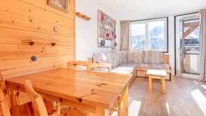 Ein gemütliches Zimmer mit einem Holztisch, Stühlen, einer Couch und einem großen Fenster mit Blick auf die Berge.
