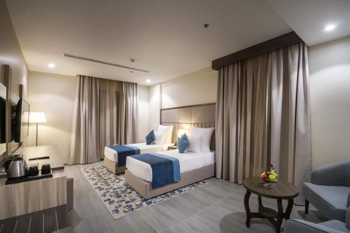 Ein Hotelzimmer mit zwei Betten, einem Schreibtisch mit Wasserkocher, einem kleinen Tisch mit Obst und einem Fernseher.