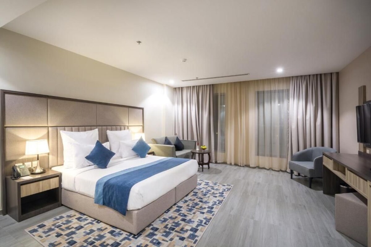A hotel room with a bed, bedside table, lamp, chair, desk, and a television.