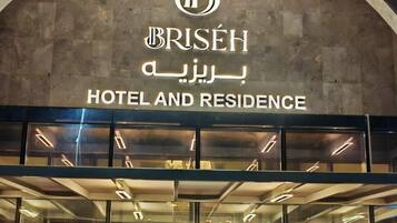 Entrada de un hotel con un amplio arco, puertas de vidrio y un letrero con el nombre del hotel en varios idiomas.
