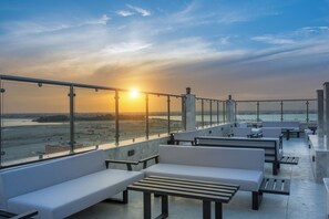 A rooftop terrace with seating areas and a view of the sunset over a body of water. - Enala AlKhobar Hotel (Al Khobar)