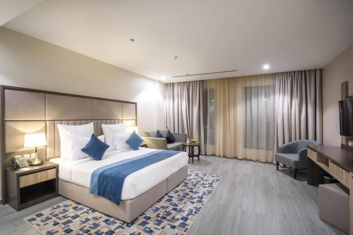 A hotel room with a bed, bedside table, lamp, chair, desk, and a television.