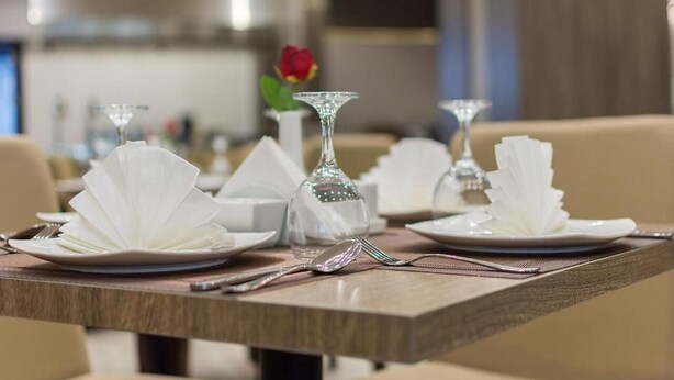 A dining table set with plates, cutlery, and a glass vase with a rose. - Briseh Hotel Alkhobar  (Al Khobar)