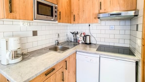 Une cuisine avec des meubles de rangement en bois, un four à micro-ondes, une machine à café, un évier et un lave-vaisselle.