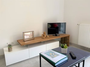 Een moderne woonkamer met een houten tv-meubel, een lijst met foto, een klein beeldje, een afstandsbediening en een boek op een tafel.