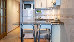 A compact kitchen with white cabinets, a microwave, a refrigerator, a sink, and two bar stools. - Central Quiet Apartment with Pool, Wi-Fi in Torredembarra (Torredembarra)