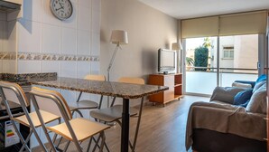 A modern living room with a sofa, a TV, and a dining area with chairs and a table. - Central Quiet Apartment with Pool, Wi-Fi in Torredembarra (Torredembarra)