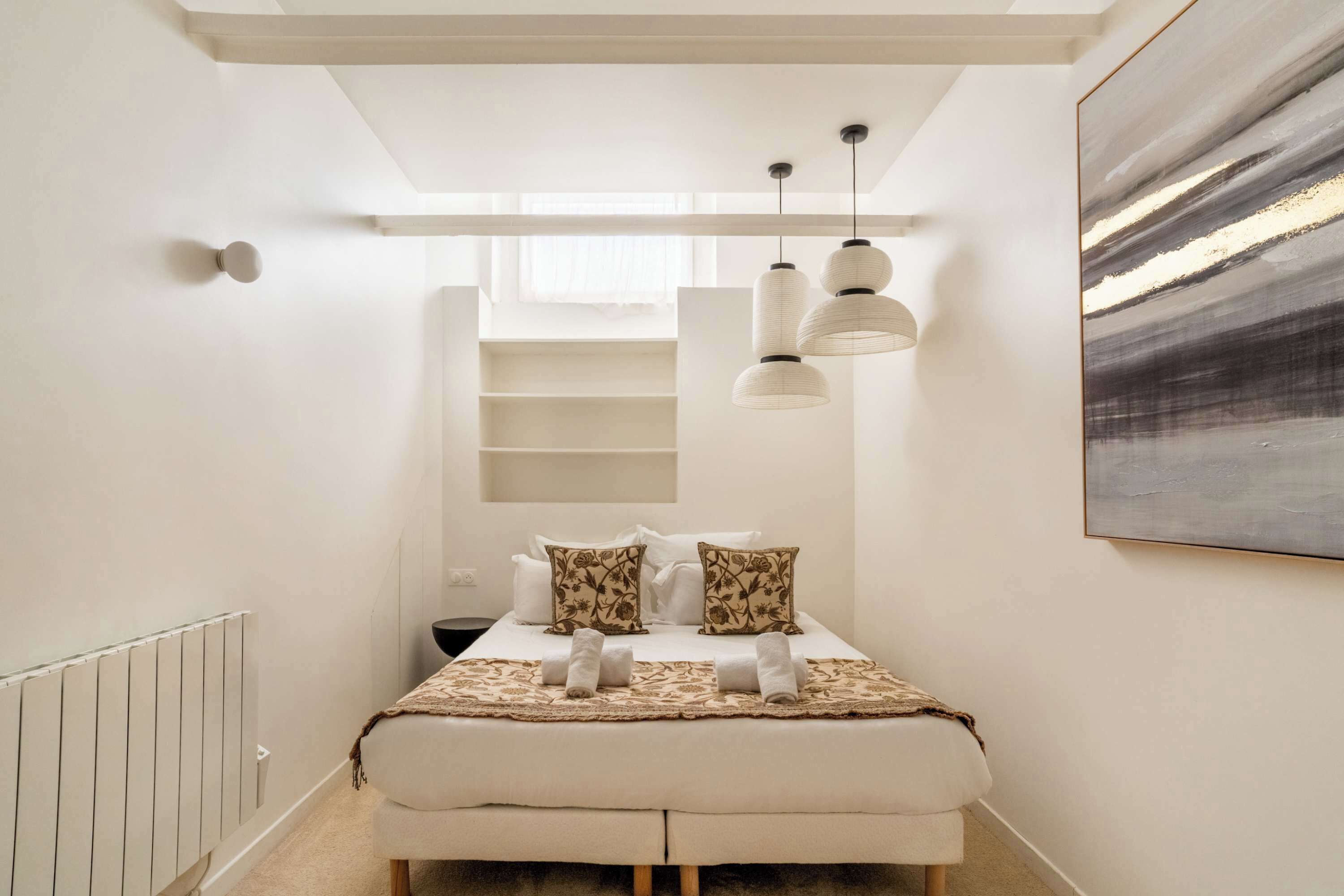 Une chambre à coucher moderne, avec un lit, des tables de chevet, un radiateur et un grand tableau abstrait accroché au mur.