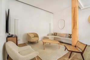 Ein modernes Wohnzimmer mit einer Couch, Sesseln, einem Couchtisch, einem Fernseher und einer Holzsäule.