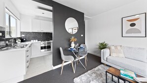 A modern kitchen with white cabinets, a black countertop, and a dining area with a glass table and chairs. - The Bluewater Nest Elwood (Elwood)